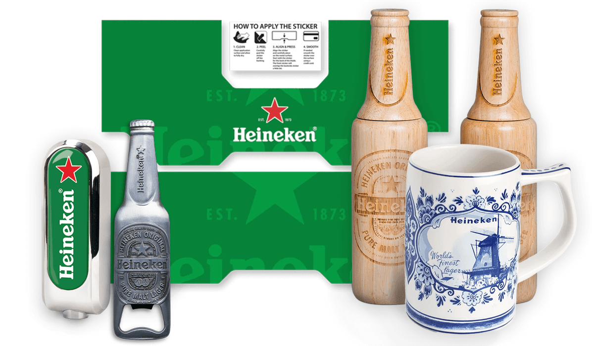 A set of Heineken branded kitchen accessories including a blue and white ceramic mug, a wooden bottle-shaped pepper and salt mill, a tap handle, stickers for the tap, and a magnetic bottle opener with a built-in bottle design.
