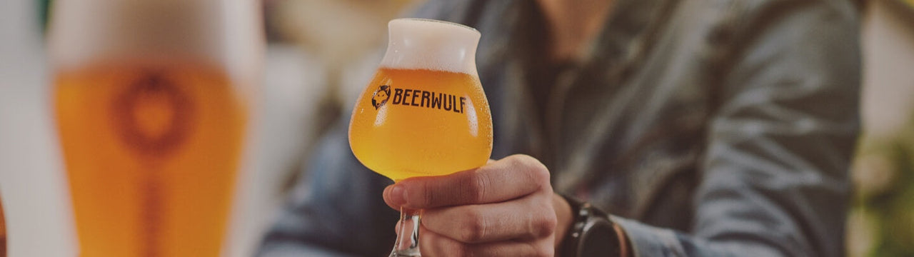 A man holding a Beerwulf glass full of beer, about to cheers another beer glass