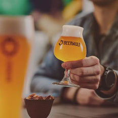 A man holding up a full glass of beer in a Beerwulf glass.