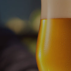 A close up shot of a glass of beer with a large foam head and water drops on the side of the glass.
