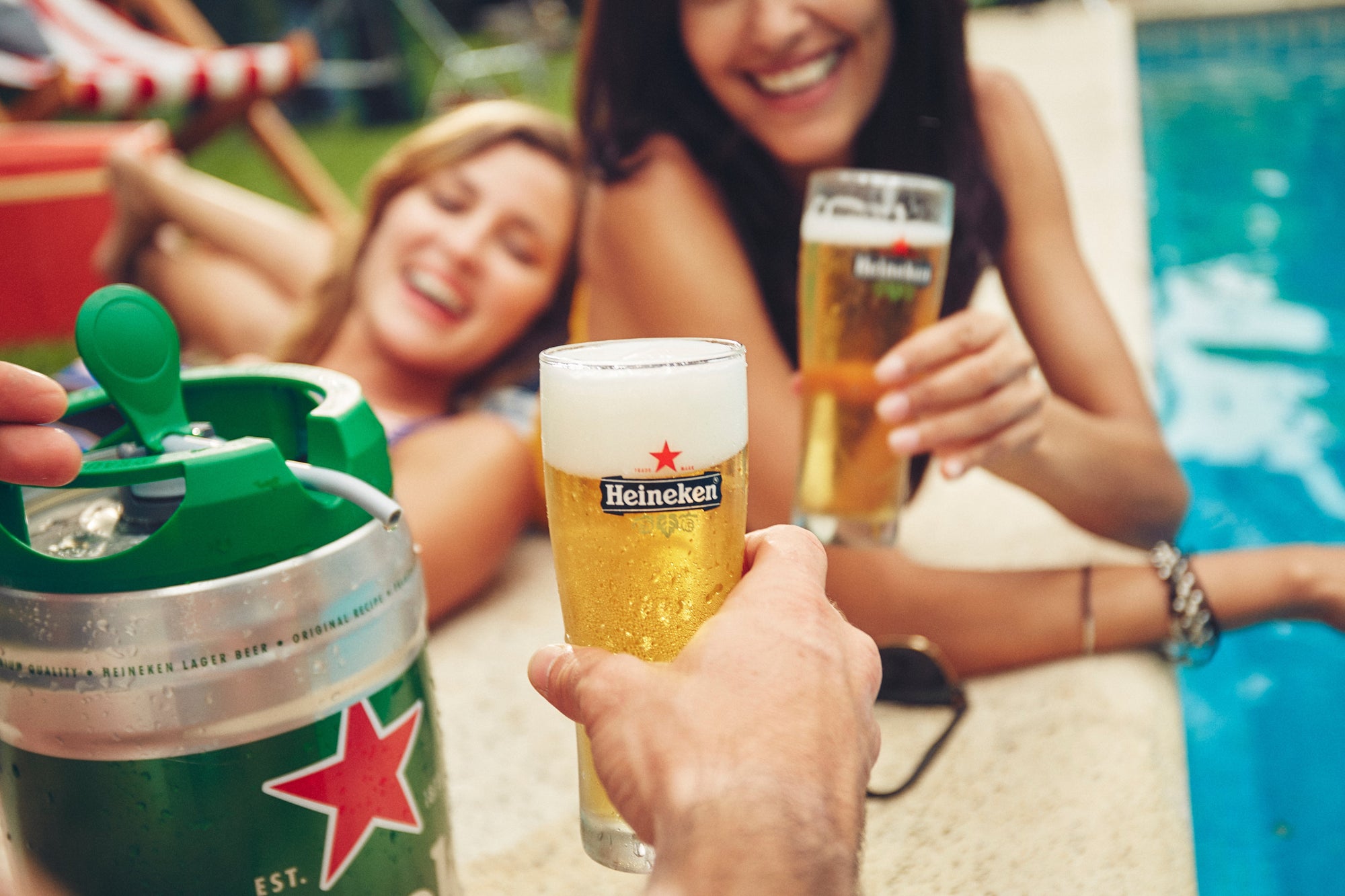 Two people enjoying Heineken beer by a poolside.
