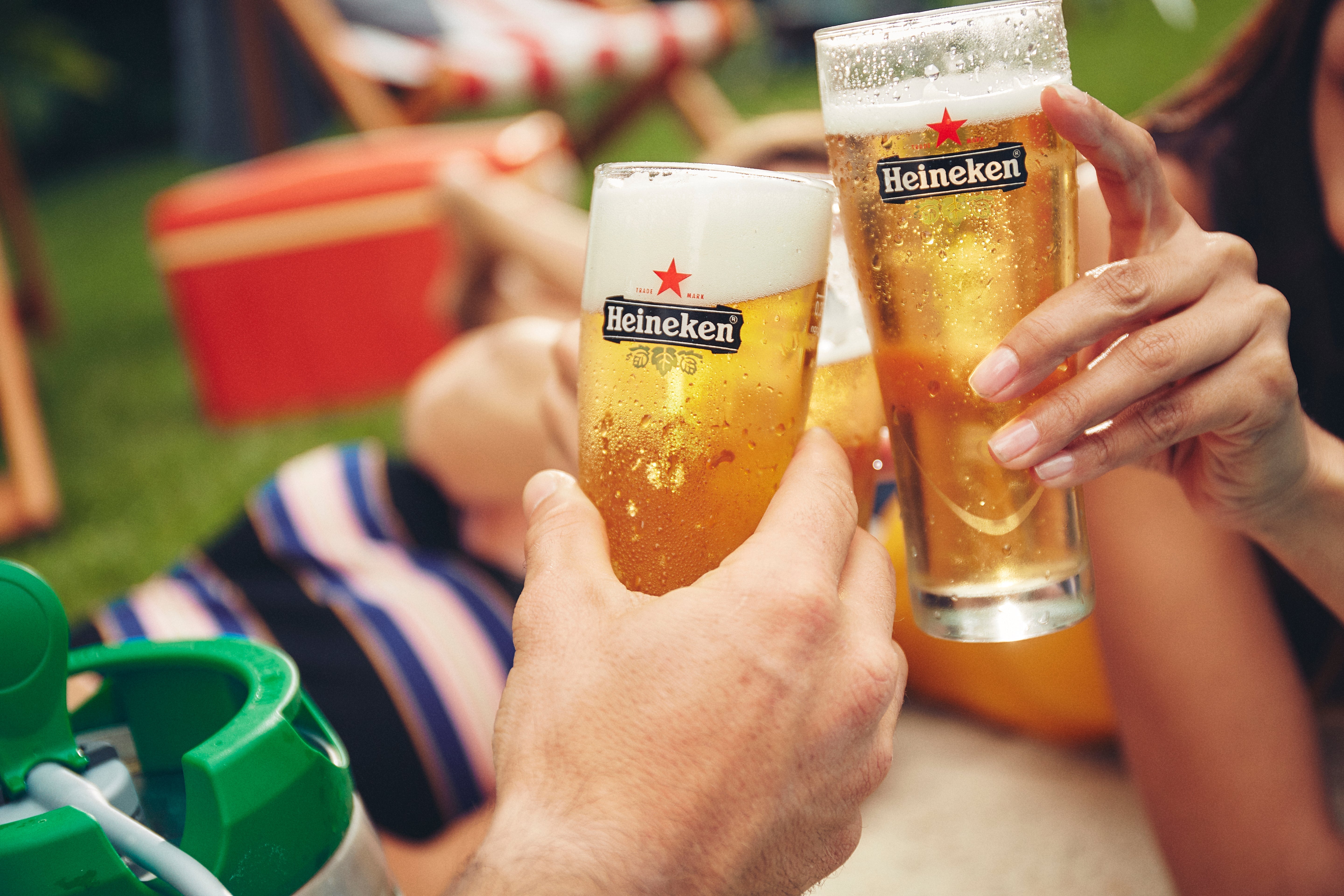 Two Heineken glasses being held up with a casual outdoor setting in the background.