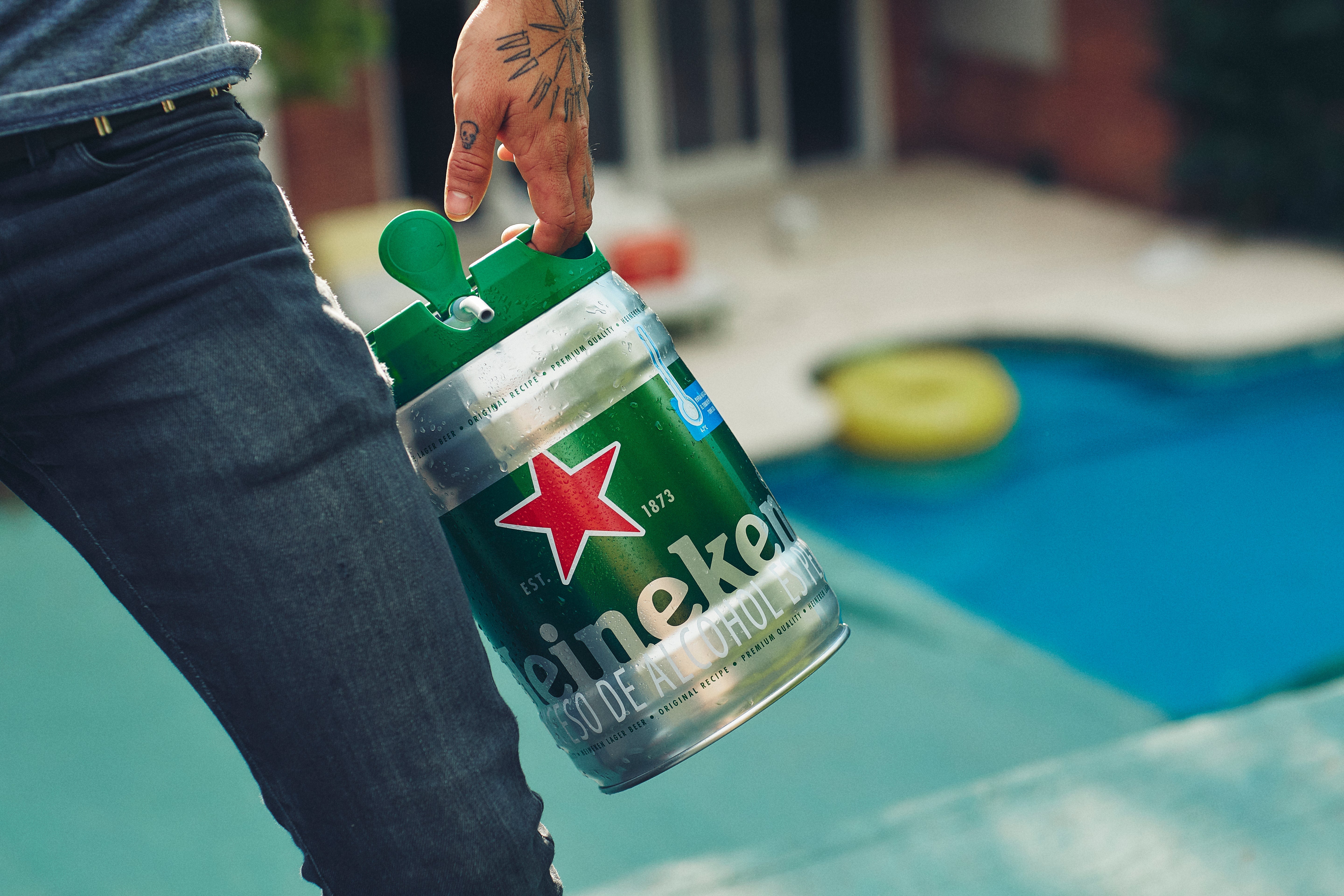Une personne tenant un fût de bière Heineken au bord d'une piscine