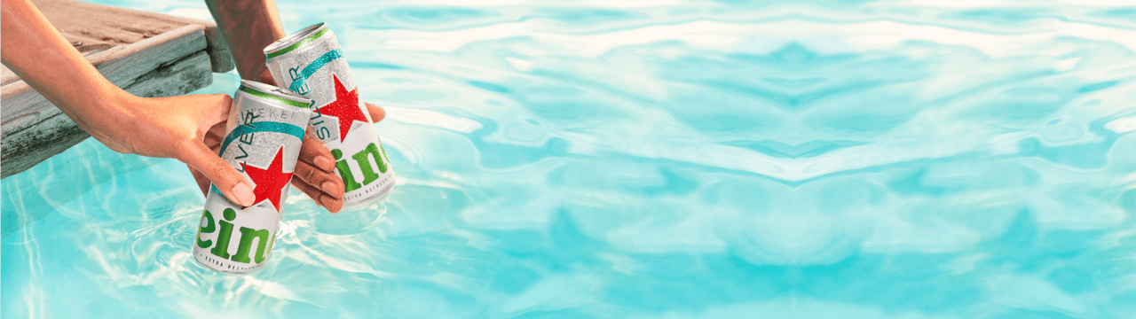 Two cans of Heineken Silver held above bright blue swimming pool water.