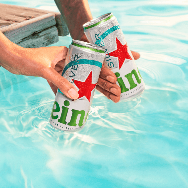 Deux canettes de Heineken Silver brandies au-dessus de l'eau bleu vif d'une piscine.
