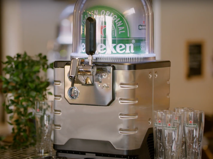 A BLADE beer machine with a Heineken keg in it and some Heineken beer glasses around it.