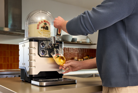 A person pouring a glass of beer from a BLADE beer machine with Birra Moretti beer keg inside