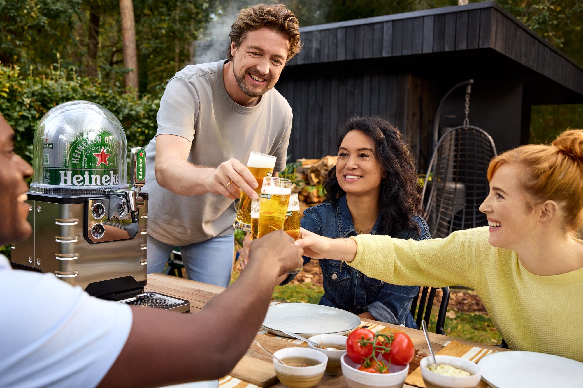 A group of people cheers with glasses of beer outdoors at a table with a BLADE beer tap on it.