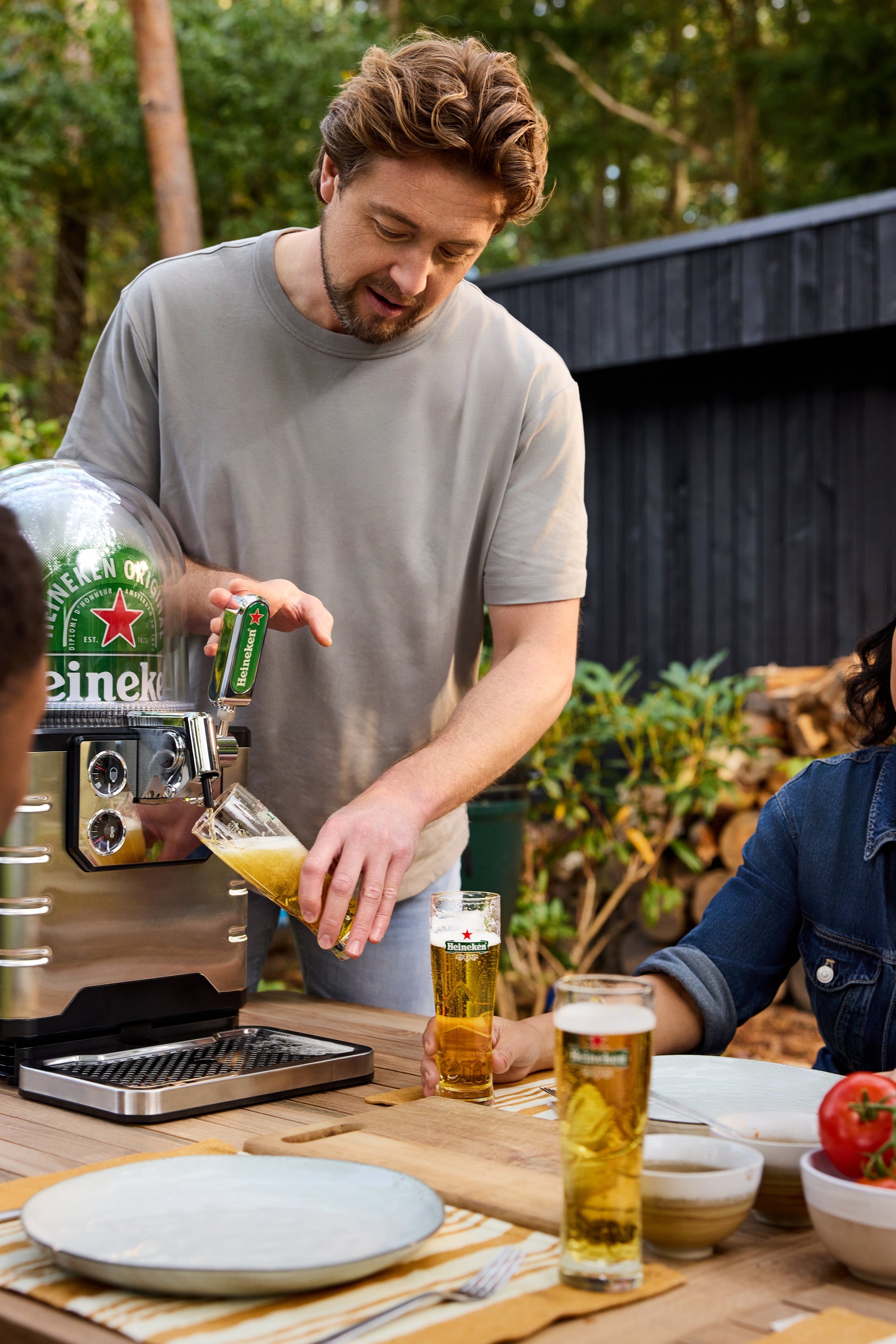 Man pouring Heineken beer at an outdoor table with a garden background