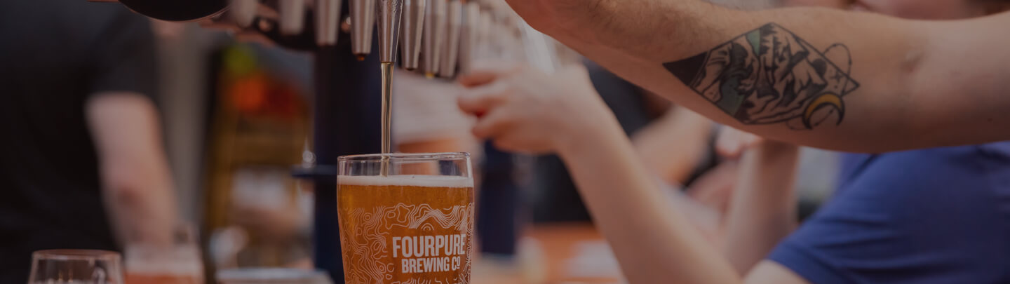 A person pours a draught beer into a Fourpure glass from a line of beer taps in a bar.