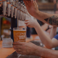 A person pours a draught beer into a Fourpure glass from a line of beer taps in a bar.