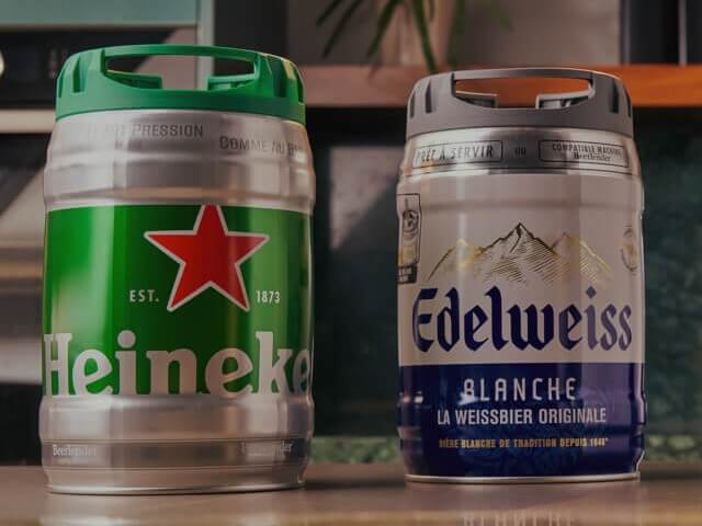 A Heineken and Edelweiss beer keg lined up next to each other on a table.