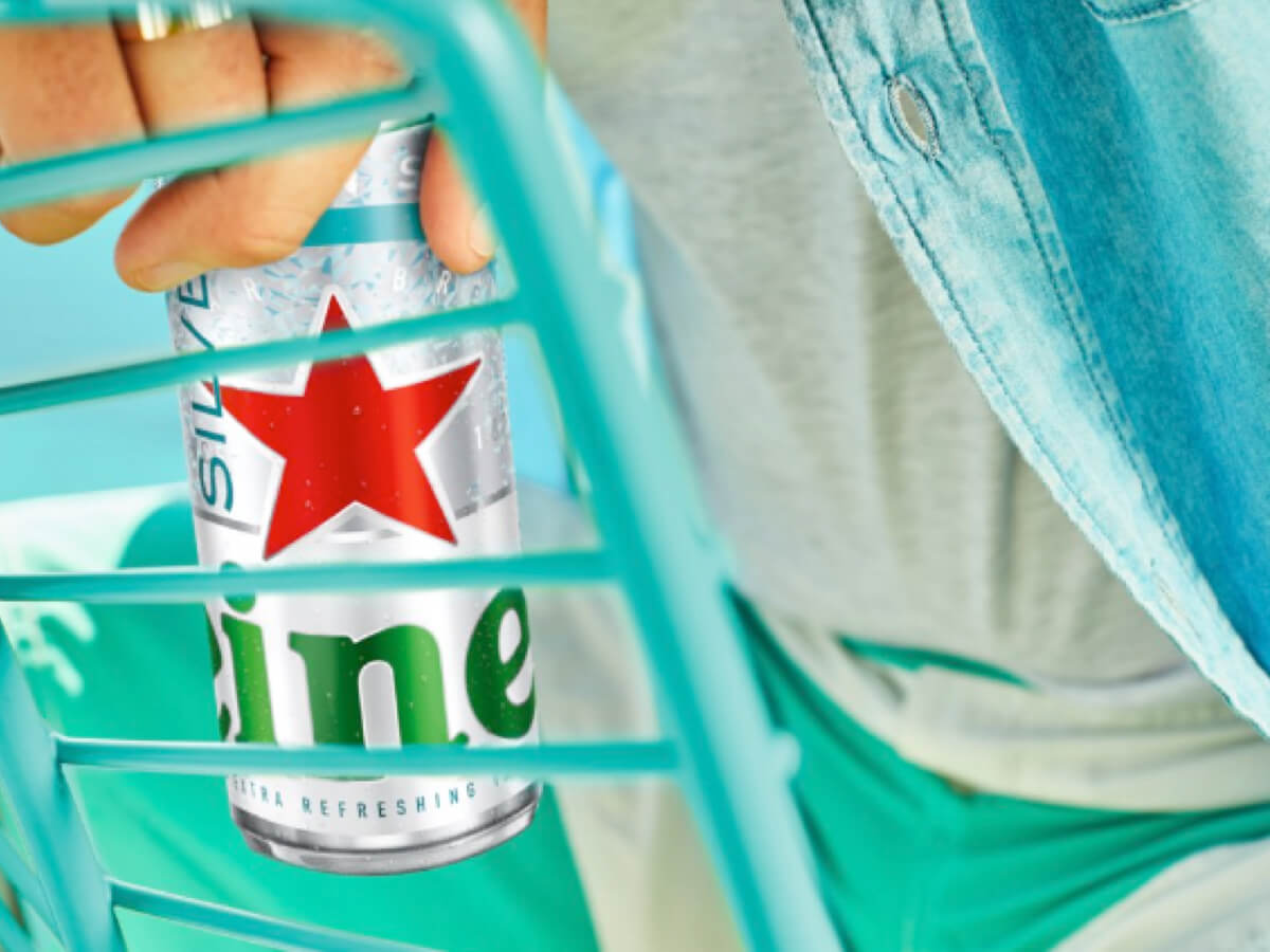 Une personne vêtue d'une chemise bleue tient une canette de bière Heineken Silver bien fraîche.