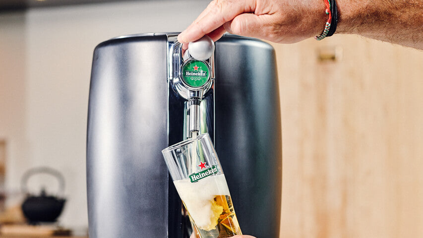 A person pouring a Heineken beer from a BeerTender beer machine into a Heineken glass.