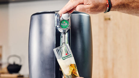 A person pouring a Heineken beer from a BeerTender beer machine into a Heineken glass.