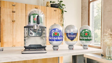 A BLADE beer machine on a table with a Heineken keg inside and a Heineken, Affligem & Heineken 0.0 BLADE keg lined up in a row next to it.