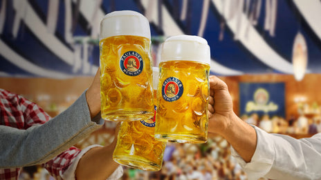 Three people cheers with steins of Paulaner beer at the Oktoberfest beer festival.