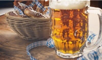 A stein of beer next to a basket of pretzels decorated with a blue ribbon.