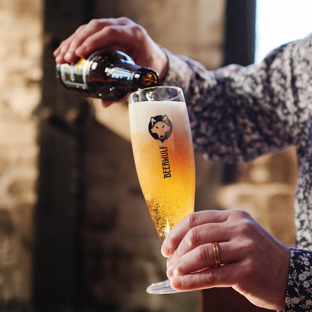 Someone pouring a beer from a bottle into a high Beerwulf glass